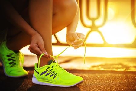 woman tying running shoes on running path beside road
