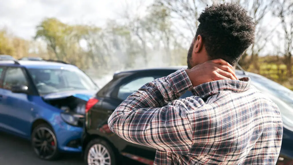 A man holding his neck while looking at two cars involved in a recent accident, likely to file for a personal injury lawsuit.