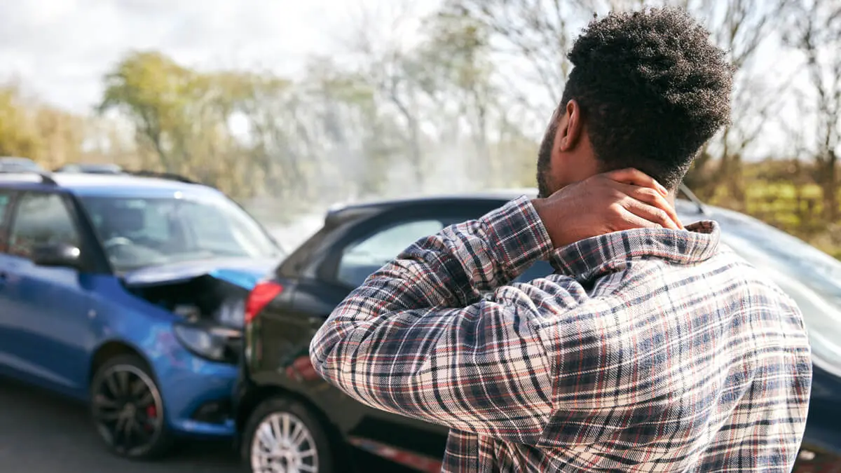 A man holding his neck while looking at two cars involved in a recent accident, likely to file for a personal injury lawsuit.